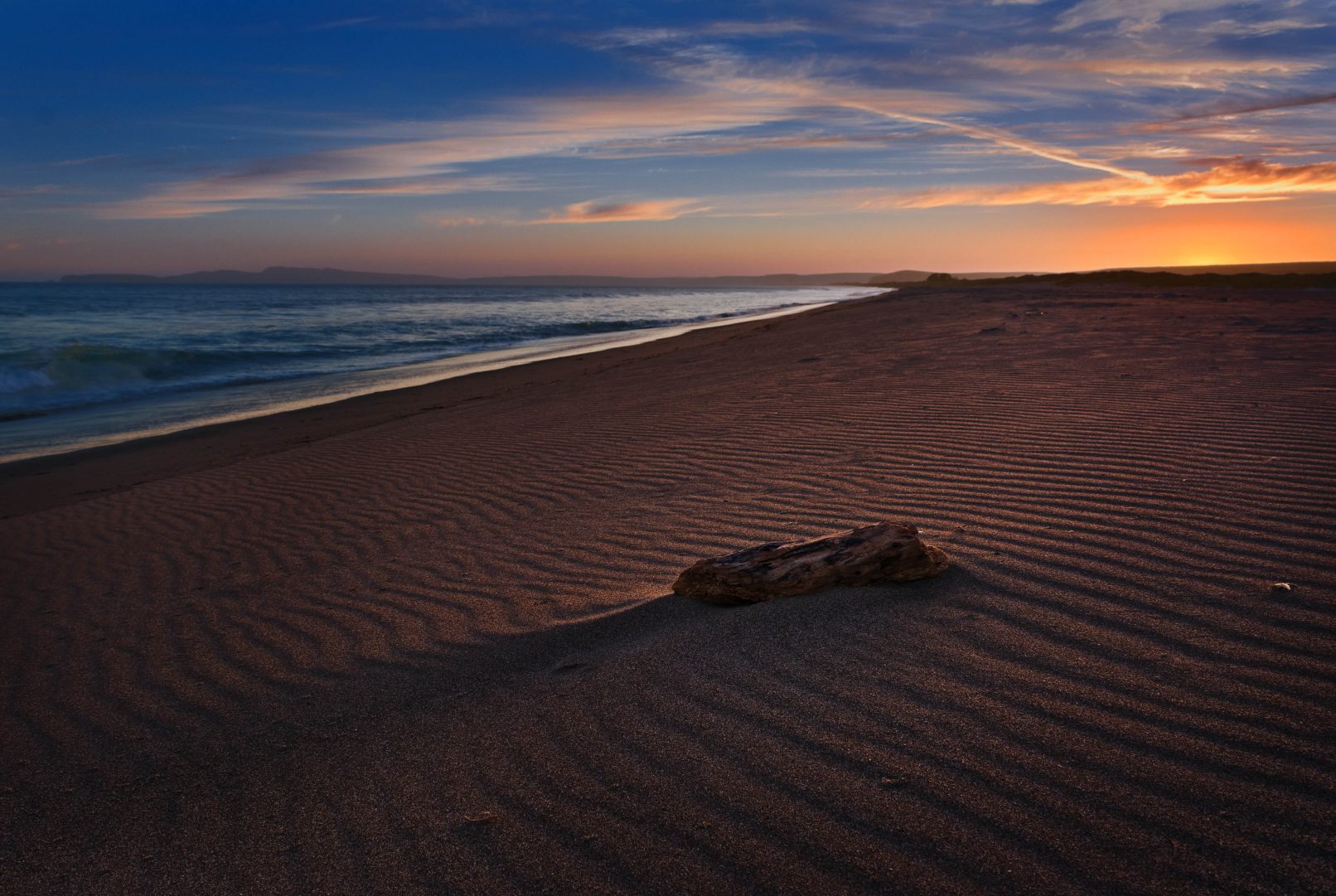 Beach sunset with wood and ridges in sand