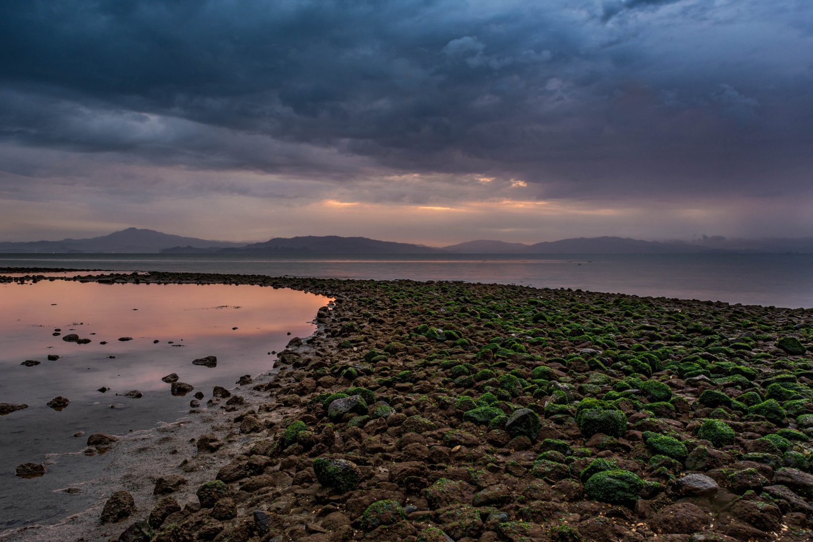 San Pablo Bay from Point Pinole, California with moss covered rocks and stormy, dark clouds